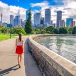 Sydney,City,Girl,Tourist,Walking,In,Urban,Park,With,Skyscrapers