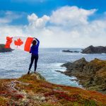 Adventurous,Woman,Holding,A,Canadian,Flag,On,A,Rocky,Atlantic